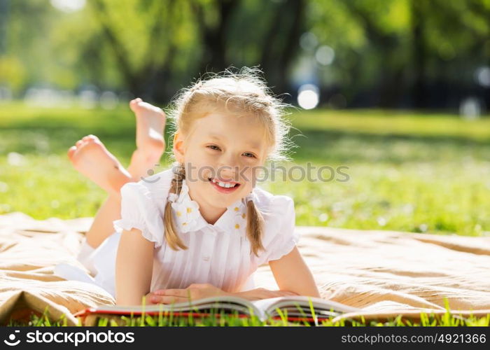 Weekend in park. Little cute girl in summer park reading book