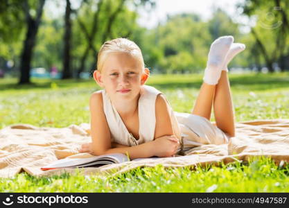 Weekend in park. Little cute girl in summer park reading book