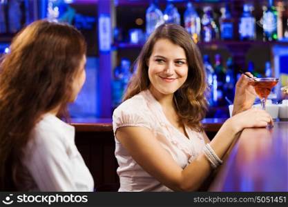 Weekend party. Two young pretty women a bar drinking cocktails