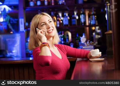 Weekend party. Young attractive lady at bar talking on phone