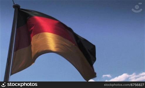 Wehende Deutschlandflagge vor blauem Himmel teils im Schattenlicht, teils in leuchtenden Farben