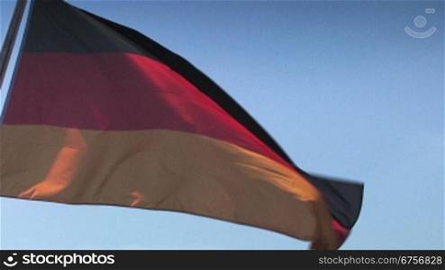 Wehende Deutschlandflagge vor hellblauen Himmel in leuchtenden Farben, teils im Schattenlicht