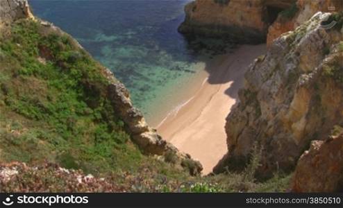 Wei?er verlassener Natursandstrand vor tnrkisblauem Wasser zwischen hohen, steilen, teilweise grnn bewachsenen sandsteinfarbenen Felsen / Klippen - Knste der Algarve, Portugal.