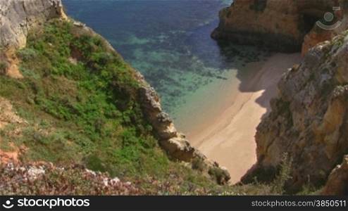 Wei?er verlassener Natursandstrand vor tnrkisblauem Wasser zwischen hohen, steilen, teilweise grnn bewachsenen sandsteinfarbenen Felsen / Klippen - Knste der Algarve, Portugal.