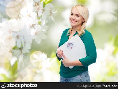 weight loss, diet, slimming, plus size and people concept - smiling young woman holding scales over natural cherry blossom background