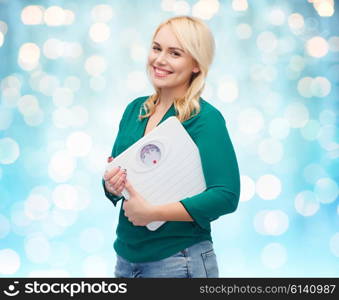 weight loss, diet, slimming, plus size and people concept - smiling young woman holding scales over blue holidays lights background