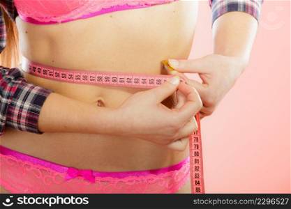 Weight loss, healthy lifestyle concept. Closeup measuring tape on woman body, fit girl wearing pink lace lingerie measuring her waistline