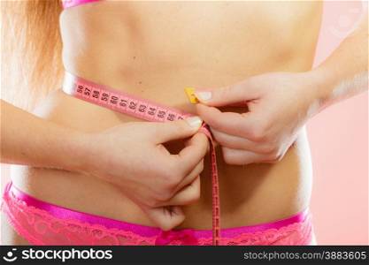 Weight loss, healthy lifestyle concept. Closeup measuring tape on woman body, fit girl wearing pink lace lingerie measuring her waistline