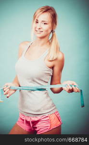 Weight loss, slim body, healthy lifestyle concept. Fit fitness girl measuring her waistline with measure tape on blue