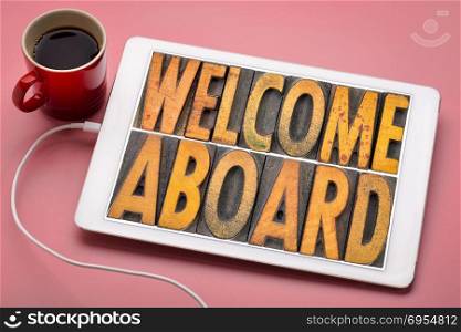 welcome aboard banner in vintage letterpress wood type blocks stained by color inks on a digital tablet with a cup of coffee