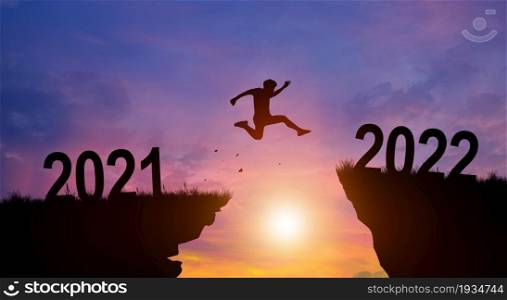 Welcome merry Christmas and Happy new year in 2022. Man jumping across the gap from 2021 to 2022 cliff with Sunset and Twilight Sky background.