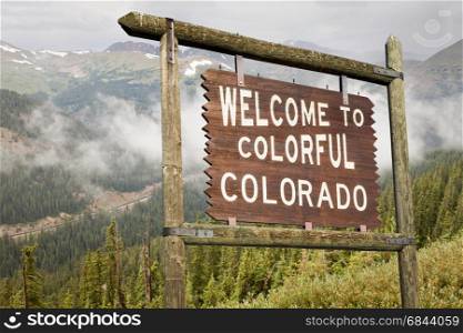 welcome to colorful Colorado roadside wooden sign with Rocky Mountains in background