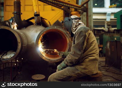 Welder in mask works with big metal pipe on factory, welding skill. Metalworking industry, industrial manufacturing of steel products. Welder works with metal on factory, welding skill