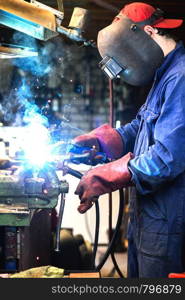 welder is welding metal part in garage. with protective mask, industrial steel welder work. welder is welding metal part in garage. with protective mask, industrial steel welder