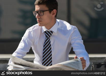 Well dressed business man reading newspaper sitting on a street sidewalk