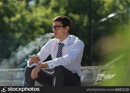 Well dressed business man smoking sitting on a street sidewalk