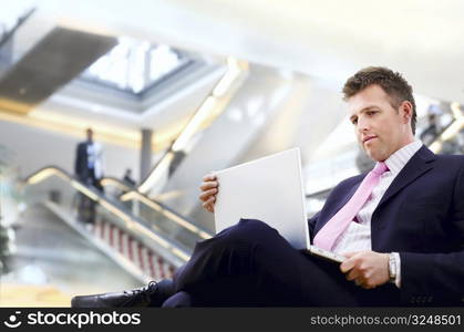 Well dressed businessman sitting in the lobby and using laptop computer.