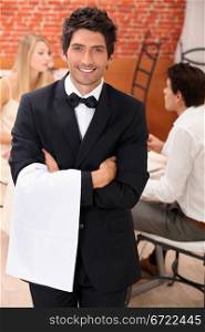 well dressed waiter facing the camera, behind a couple is dining at restaurant