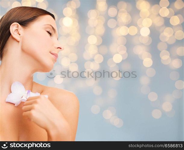 wellness and beauty concept - beautiful bare woman with orchid flower over holidays lights background. woman with orchid flower over green background
