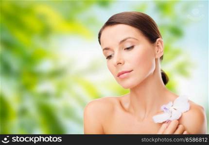 wellness and beauty concept - beautiful woman with orchid flower over green natural background. woman with orchid flower over green background