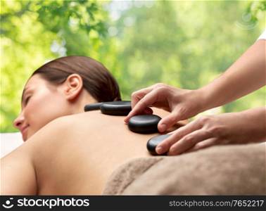 wellness, beauty and bodycare concept - close up of woman having hot stone massage at spa over green natural background. close up of woman having hot stone massage at spa