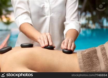 wellness, beauty and bodycare concept - close up of woman having hot stone massage at spa over tropical beach background in french polynesia. close up of woman having hot stone massage at spa