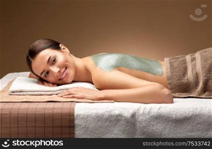 wellness, beauty and cosmetology concept - beautiful young woman lying with blue clay mask on back at spa. woman with blue clay mask on back in spa
