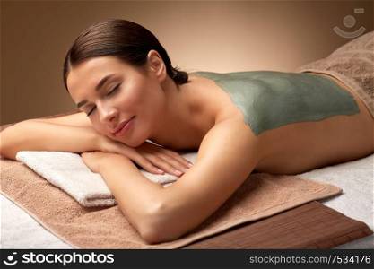 wellness, beauty and cosmetology concept - beautiful young woman lying with blue clay mask on her back at spa. woman with blue clay mask on her back at spa