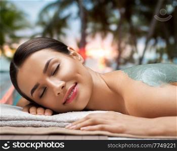 wellness, beauty and cosmetology concept - beautiful young woman lying with blue clay mask at spa over tropical beach background in french polynesia. woman with blue clay mask in spa