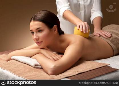 wellness, beauty and relaxation concept - beautiful young woman having back massage with sponge at spa. woman having back massage with sponge at spa
