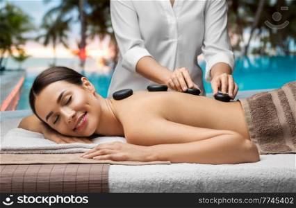 wellness, beauty and relaxation concept - beautiful young woman having hot stone massage at spa over tropical beach background in french polynesia. beautiful woman having hot stone massage at spa