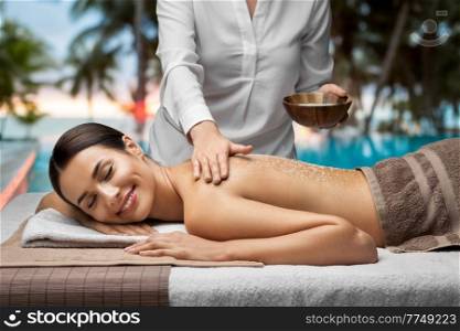 wellness, beauty and relaxation concept - beautiful young woman having salt massage at spa over tropical beach background in french polynesia. beautiful young woman having salt massage at spa