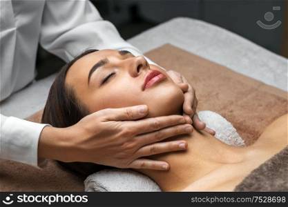 wellness, beauty and relaxation concept - beautiful young woman lying with closed eyes and having face and head massage at spa. woman having face and head massage at spa