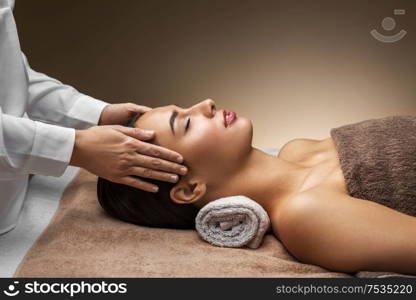 wellness, beauty and relaxation concept - beautiful young woman lying with closed eyes and having face and head massage at spa. woman having face and head massage at spa