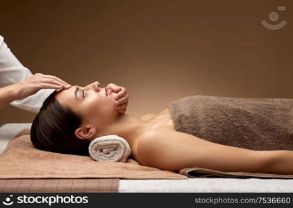 wellness, beauty and relaxation concept - beautiful young woman lying with closed eyes and having face and head massage at spa. woman having face and head massage at spa