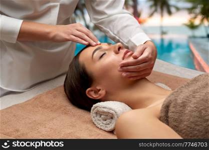 wellness, beauty and relaxation concept - beautiful young woman lying with closed eyes and having face and head massage at spa over tropical beach background in french polynesia. woman having face and head massage at spa