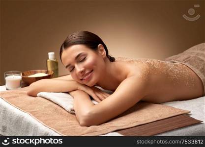wellness, beauty and relaxation concept - beautiful young woman lying with exfoliating sea salt scrub on skin of her back at spa. woman lying with sea salt scrub on skin at spa