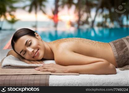 wellness, beauty and relaxation concept - beautiful young woman lying with sea salt on skin at spa over tropical beach background in french polynesia. woman lying with sea salt on skin at spa
