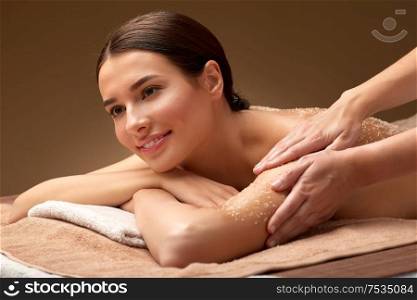 wellness, beauty and relaxation concept - happy young woman having exfoliating salt massage at spa. happy woman having exfoliating salt massage at spa