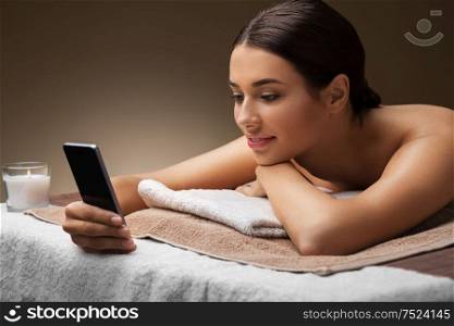 wellness, beauty and relaxation concept - young woman lying at spa or massage parlor. woman with smartphone at spa or massage parlor