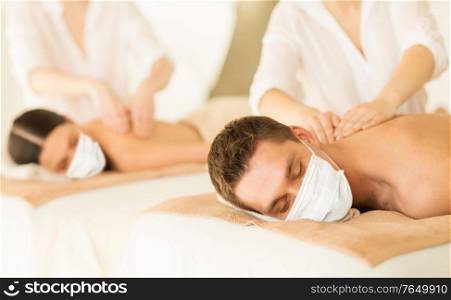 wellness, bodycare and health concept - couple wearing face protective medical mask for protection from virus disease having back massage at spa. couple in masks having back massage at spa