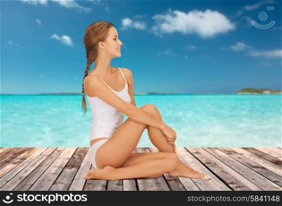 wellness, health and people concept - beautiful young woman in cotton underwear sitting on wooden floor over sea and blue sky background