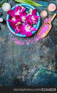 Wellness or spa background with pink orchid flowers in bowl with water, shovel of sea salt, cream jar , candles and green bamboo leaf . Top view, place for text.