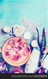 Wellness setting with orchid flowers floating in bowl of water and spa tools on turquoise shabby chic background, top view. Pastel toned