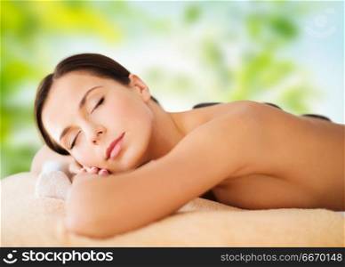 wellness, spa and beauty concept - beautiful woman having hot stone therapy over green natural background. beautiful woman having hot stone therapy at spa. beautiful woman having hot stone therapy at spa