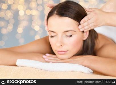 wellness, spa and beauty concept - close up of beautiful woman having head massage over holidays lights background. close up of beautiful woman having head massage