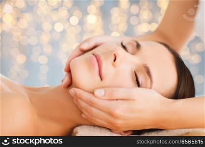 wellness, spa and beauty concept - close up of beautiful woman having face massage over holidays lights background. close up of beautiful woman having face massage