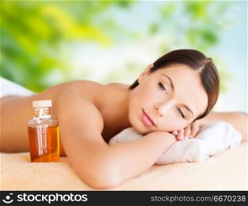wellness, spa and beauty concept - close up of beautiful woman with bottle of massage or essential oil over green natural background. close up of beautiful woman having massage at spa. close up of beautiful woman having massage at spa