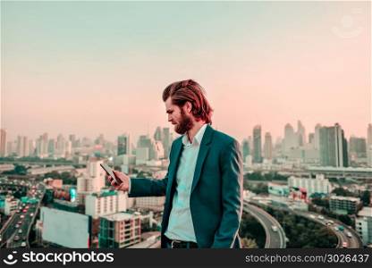 Western businessman using a phone on a rooftop with blurry city . Western businessman using a phone on a rooftop with blurry city background. Western businessman using a phone on a rooftop with blurry city background