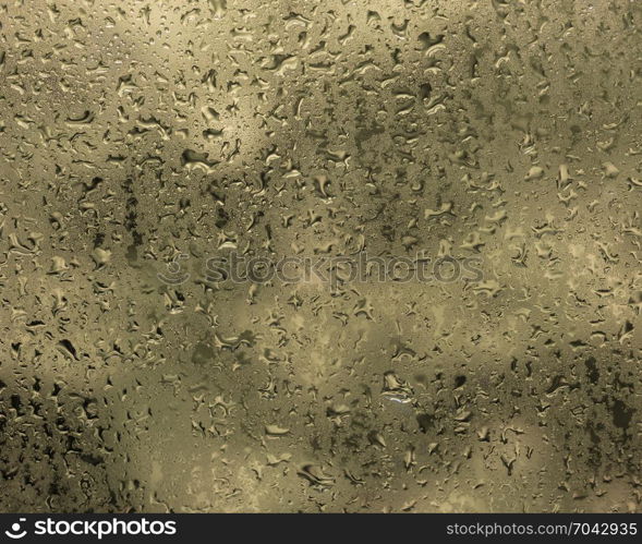 wet drops of water against glass pane with warm colored background